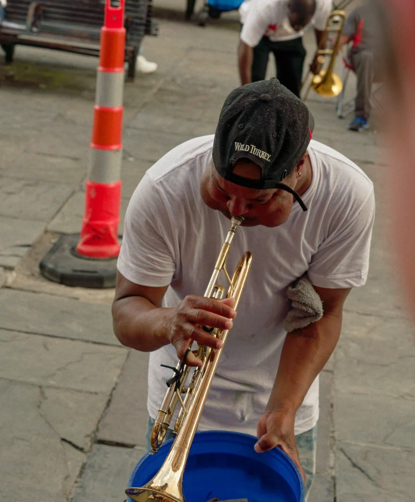 Man playing a trumpet with one hand and holding a blue bucket with the other