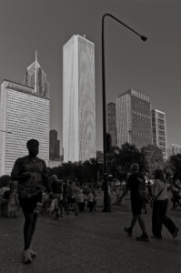 Tall buildings in Downtown Chicago in the late afternoon light. Man in the foreground with other people around and a single light post silhouetted against the sky between the buildings.