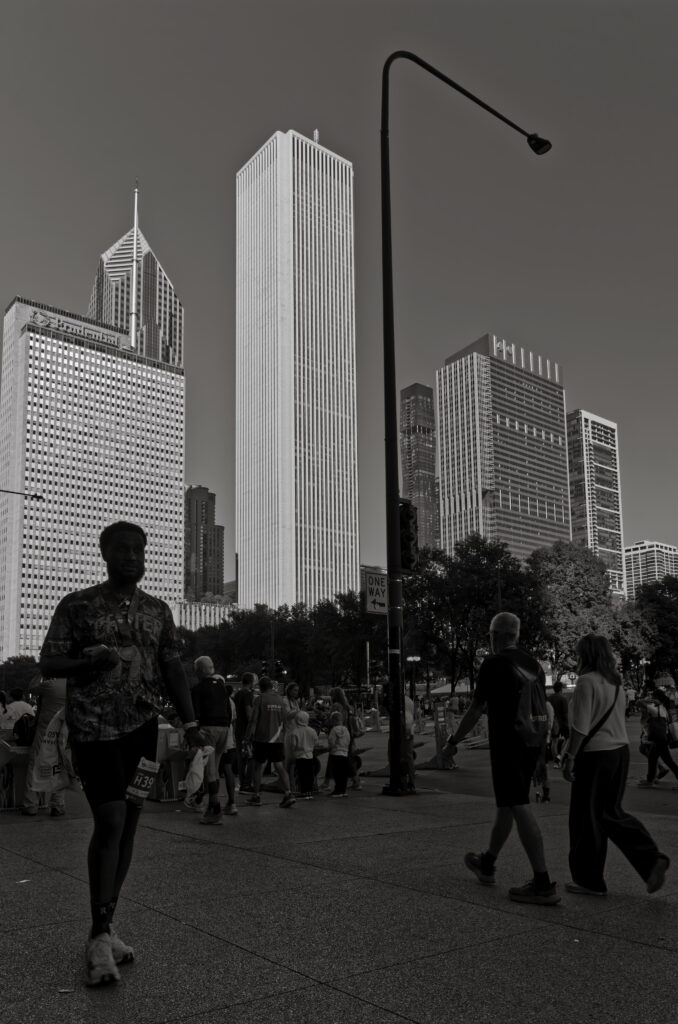 Tall buildings in Downtown Chicago in the late afternoon light. Man in the foreground with other people around and a single light post silhouetted against the sky between the buildings.